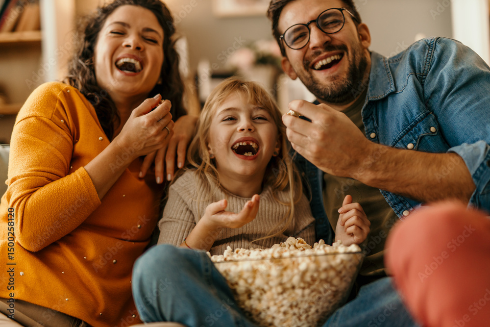 © La Famiglia - Happy family laughing and eating popcorn while watching tv © La Famiglia - Happy family laughing and eating popcorn while watching tv