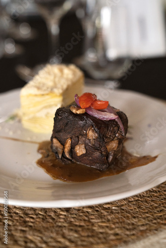 Gourmet gastronomy in a social event. Closeup view of a grilled loin fillet with sauce and a potato mille feuille in a white dish on the gala table	