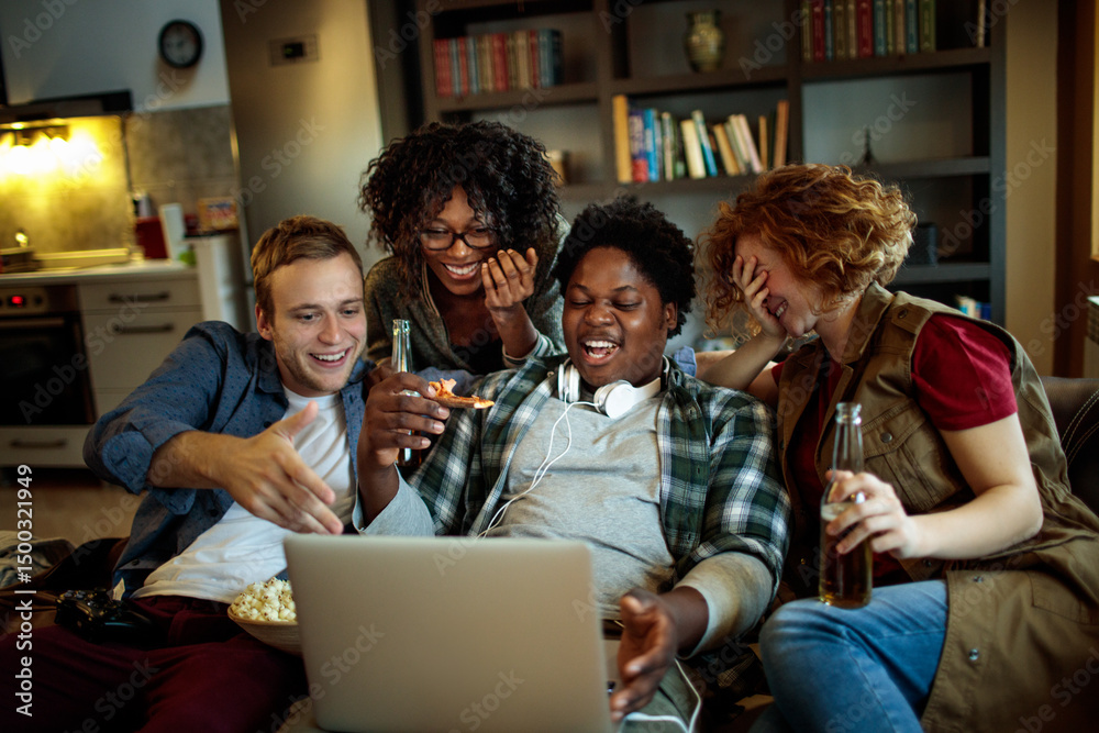 Fototapeta premium Young and diverse group of friends watching a movie on laptop in the living room on the couch