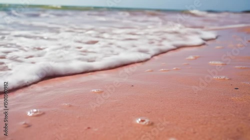 Close up view of pink sand beach with waves washing ashore on a sunny day