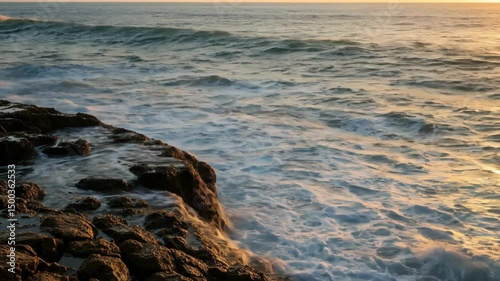Dramatic ocean waves crashing against rocky shore during a beautiful sunset light