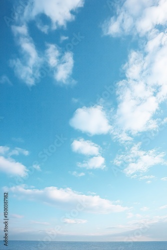 Fototapeta Naklejka Na Ścianę i Meble -  Bright blue sky with scattered white clouds over calm ocean horizon creating a peaceful and serene atmosphere