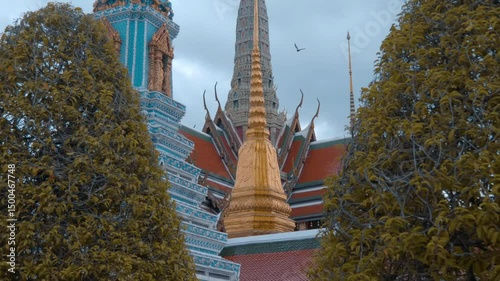Colorful picturesque spires of traditional Thai style Buddhist temples and Stupas (Chedi) covered with colorful tiles and tiny golden mirrors rise into the cloudy Bangkok sky. Shot in motion