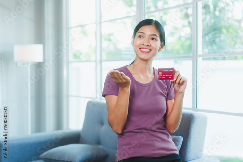 Happy Asian woman sits comfortably on a sofa,smiling while holding multiple credit cards,representing convenient online shopping,smart financial planning,modern digital consumption in a relaxed home Free Download Happy Asian woman sits comfortably on a sofa,smiling while holding multiple credit cards,representing convenient online shopping,smart financial planning,modern digital consumption in a relaxed home - GFXLoad
