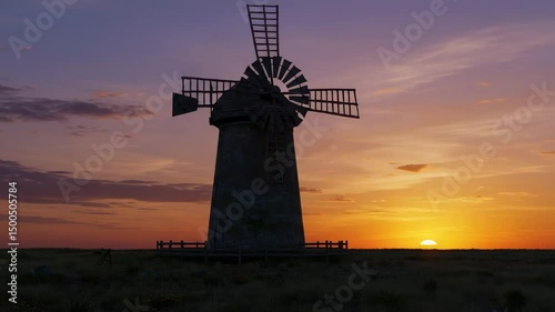 Majestic windmill vibrant sunset sky. Rustic charm meets natural beauty.Seamless looping 4k time-lapse virtual video animation background. 4k video, a windmill in a field of tall grass at sunset, 