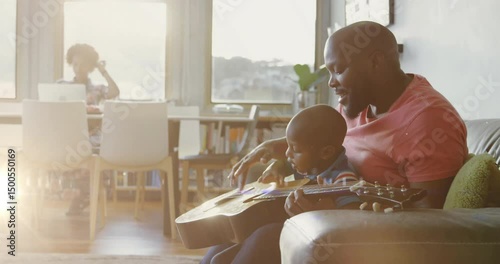 mother answering smartphone call by window, father guiding child's guitar plucking for music lesson