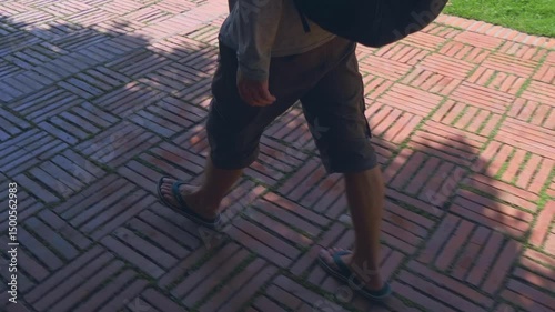 A tourist (farang) with a backpack is walking in flipflops on the red tiles of Wat Mai Chai Wichit temple grounds in Ayutthaya, Thailand. Shot in motion