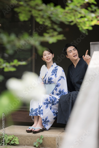 夫婦やカップルでの浴衣での温泉旅行や観光のイメージ　縁側で座る指を差して見つめる　縦　緑の前ボケあり