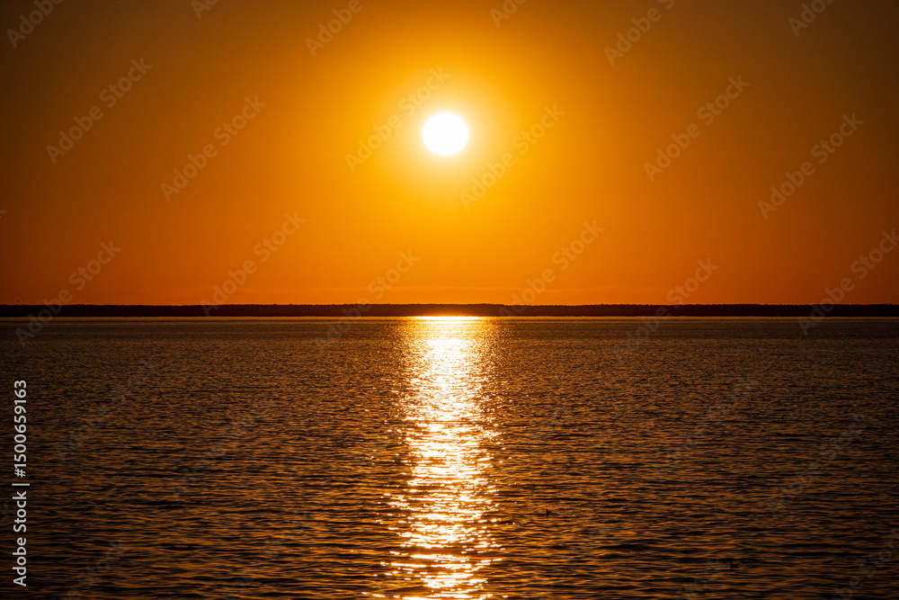 Obraz premium Radiant sunlight illuminates calm waters as the day transitions into a picturesque sunset