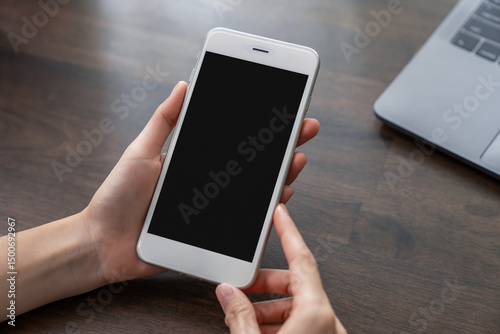 Hand holding smartphone with a blank screen on table, for putting advertising to promote.