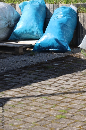 A pile of blue plastic bags sit on a brick walkway
