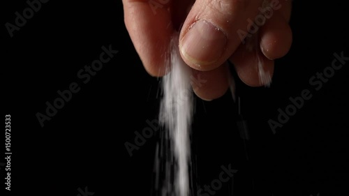 Male hand sprinkling or adding salt on black background to dish in kitchen, cooking food, slow motion. Chef adds spices
