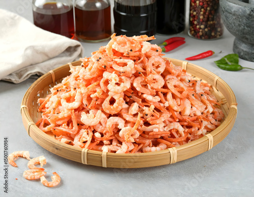 A vibrant platter of dried shrimp on a bamboo tray, surrounded by spices and sauces in a well-lit kitchen setting