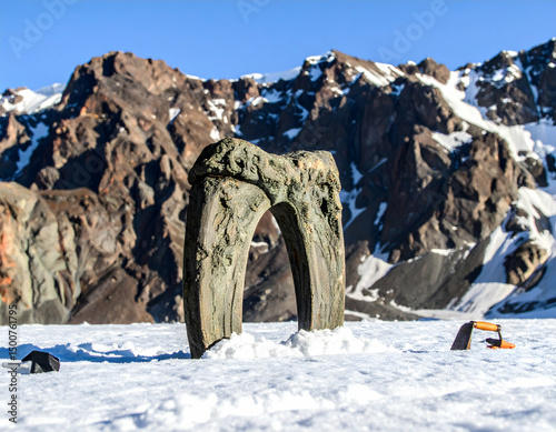 Ancient stone archway stands in a snowy landscape surrounded by majestic mountains under a clear blue sky