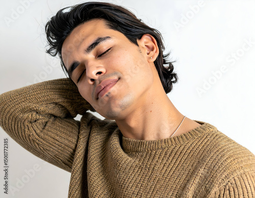 Young man in a cozy sweater relaxing with eyes closed, showcasing a serene expression against a light background