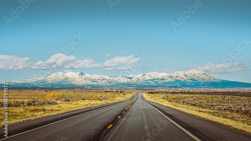 Scenic highway leading toward snow-capped mountains, blue sky