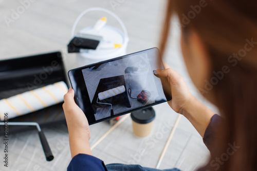 Asian woman using tablet takes photos painting supplies on floor including paint roller tray bucket brush tape measure coffee cup renovation decoration repairing home or apartment improvement concept.