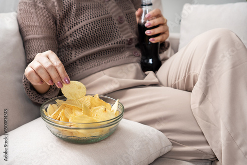 woman eating potato chips and drinking soda, showing emotional eating behavior and unhealthy food choices high in sugar and salt