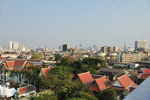 View of buildings with traditional Thai style roof and Bangkok city view at a distance.