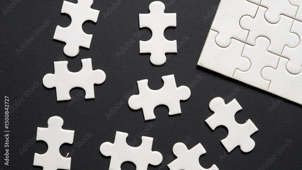 Obraz premium “Scattered white jigsaw puzzle pieces on black leather textured background. Concept image representing problem solving, decision making, strategic planning, missing piece, teamwork, or confusion.”