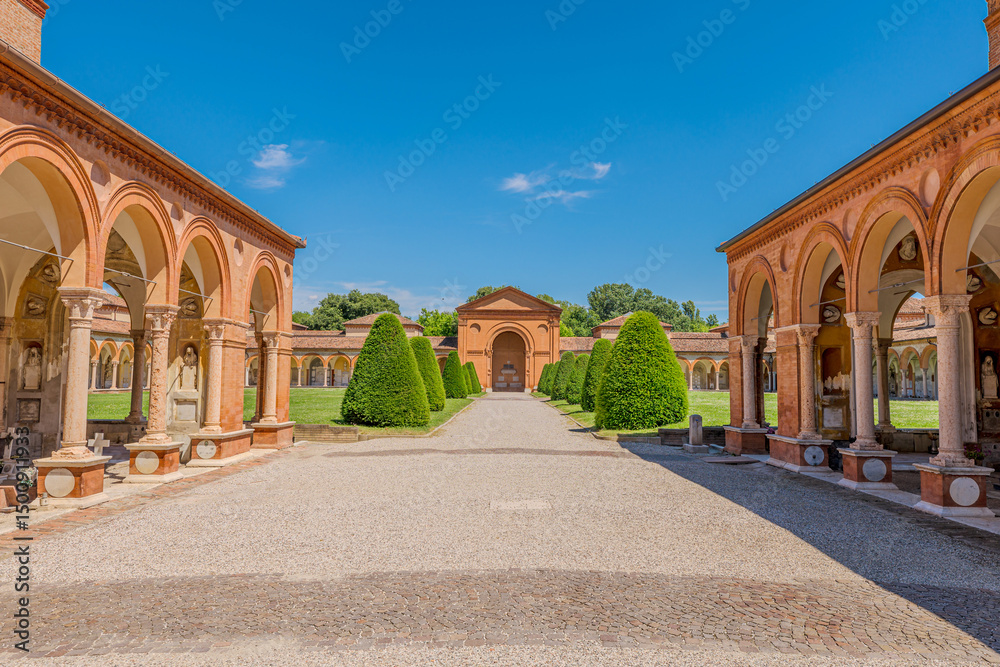 Obraz premium The 15th-century Charterhouse of Ferrara, set against a lush green lawn with San Cristoforo church. Ancient cemetery cloister featuring hanging lamps, tombs, and sculptures in Ferrara city of Italy