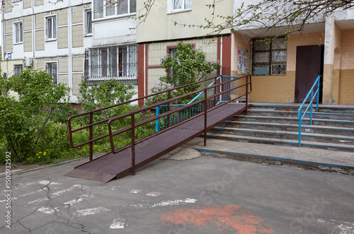 The entrance to the building is equipped with stairs and a ramp in Kyiv, Ukraine. A metal ramp, with handrails, used for wheelchairs or baby stroller to move up and down