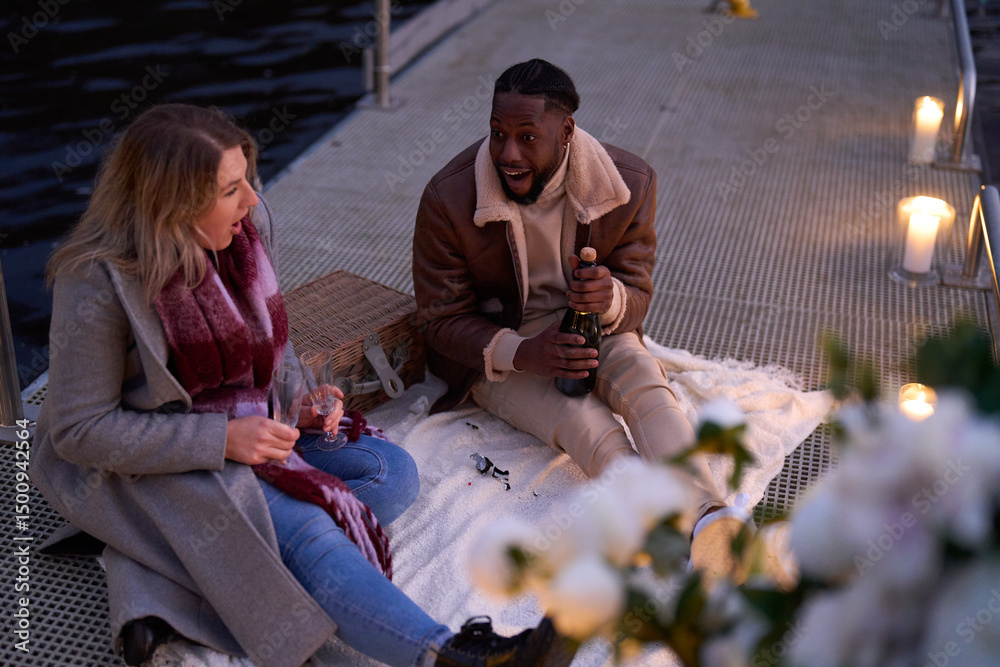 Fototapeta premium Smiling couple in warm clothing enjoying champagne on decorated pier
