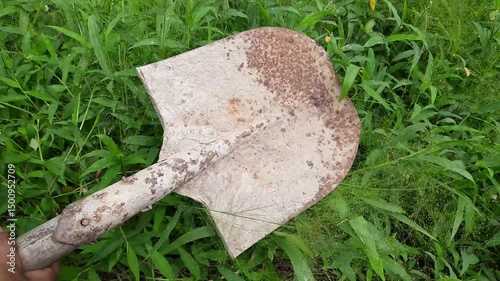 Hand Gripping Rusty, Concrete-Covered Shovel Head in Grassy Field