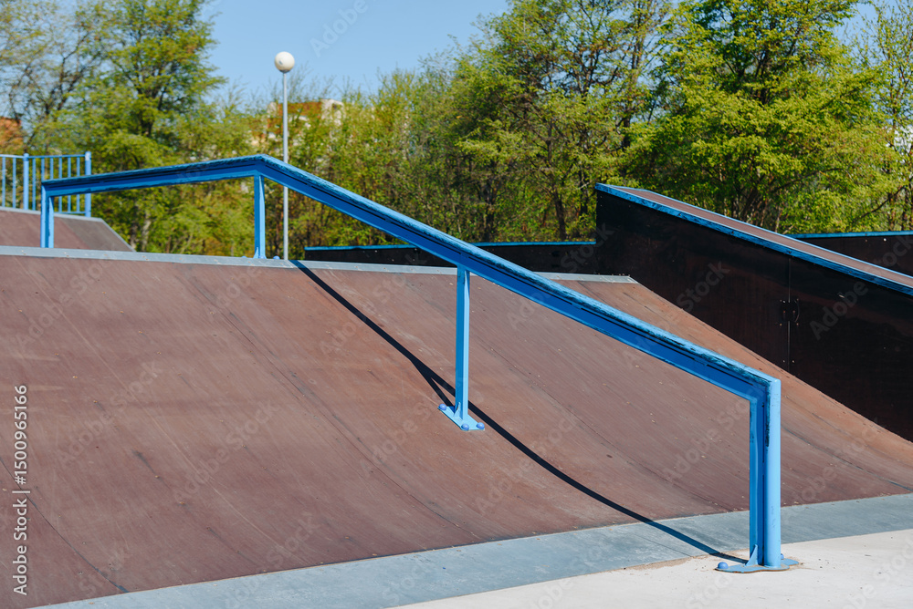 Fototapeta premium modern skate park, brown skateboard ramp with blue metal pipe outdoors in city park in summer for skateboarding, roller skating and bicycle riding, extreme sport