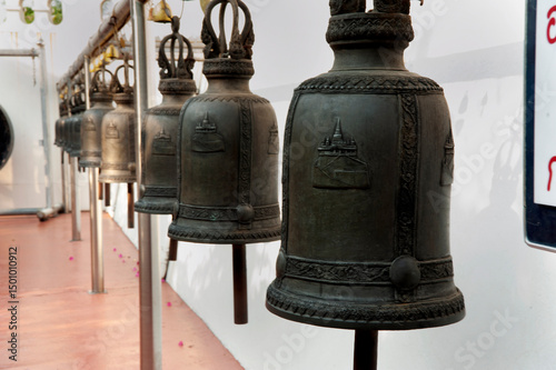 Row Of large religious bronze bells hanging next to white wall in Wat Saket Temple in Bangkok, Thailand. 
