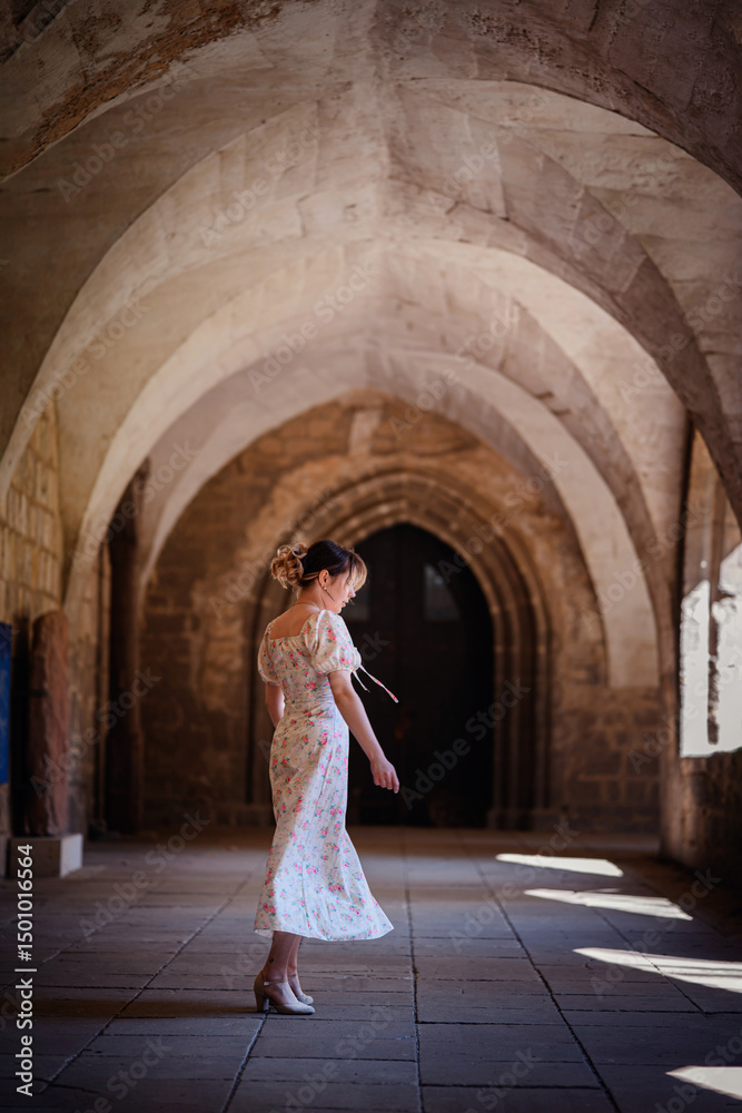 Obraz premium Woman in Floral Dress Walking Through Gothic Stone Corridor