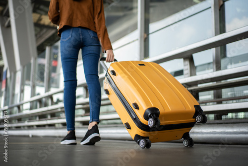 Close up of unrecognized woman tourist walking with her luggage through international airport terminal during holiday trip, female tourist rolling suitcase alone.