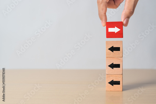 Hand putting wood cube block on top vertical red wooden blocks with white arrows facing opposite to the black arrows. With different concepts to other people. Going for success.