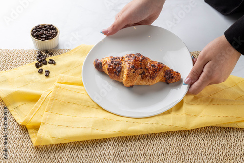 Waitress placing delicious croissant on white plate for breakfast