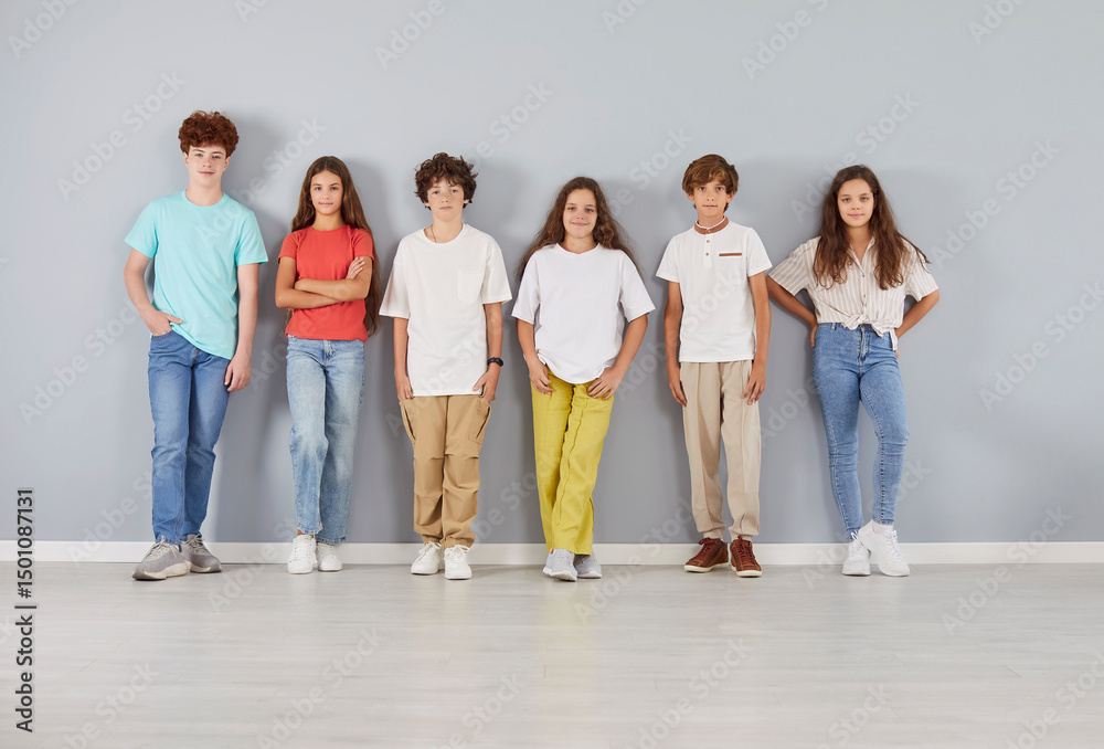 Obraz premium Group portrait of a diverse and positive team of a cheerful children, pupils and students stands together on a grey background. They are happy and united, showing friendship and teamwork.