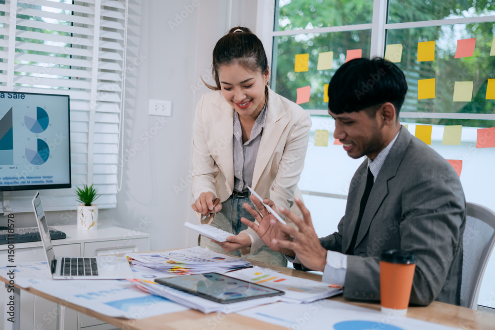 Fototapeta premium Cheerful Asian businessman and woman looking at laptop screen, analyzing and celebrating good news or project success in office.