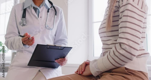 Portrait of female doctor talking with young patient sitting on couch in clinic. Physician giving consultation a woman during medical examination in office. Medicine and treatment concept. 4k video.