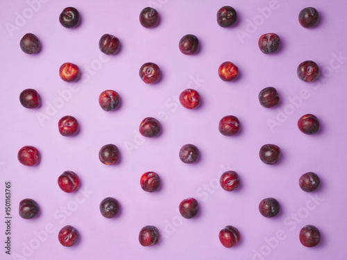 Fresh plums aligned in rows on a solid purple background. Flatlay of organic fruits from top view. 