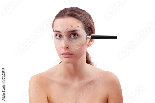 Woman portrait with no makeup, her eye examined under a magnifying glass. Authentic female face with real skin, acne, and blemishes before skincare or beauty treatment, isolated on a background