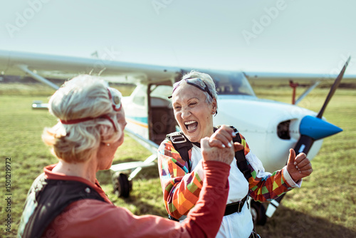 A senior lesbian couple stands on a field, airplane in the backdrop, beaming with pride and exhilaration after skydiving. Their smiles hint at a bucket list dream fulfilled. photo