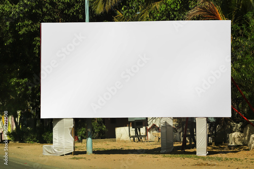 Fototapeta Naklejka Na Ścianę i Meble -  billboard on city road, outdoor advertising, mockup billing board in front of green tree and Blank white background for branding design large hoarding, Outdoor advertising construction. india.