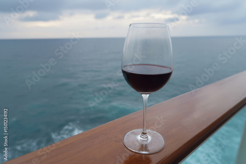 Intriguing crimson wine glass poised over tranquil ocean waves, whispers of Mediterranean escape, celebrating Bacchanalia and Ocean Day