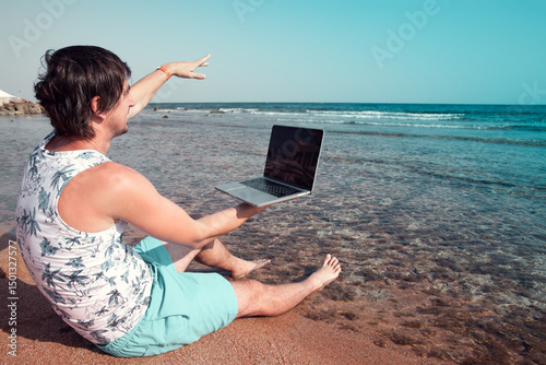 freelancer with a laptop works on a beach and waving hello