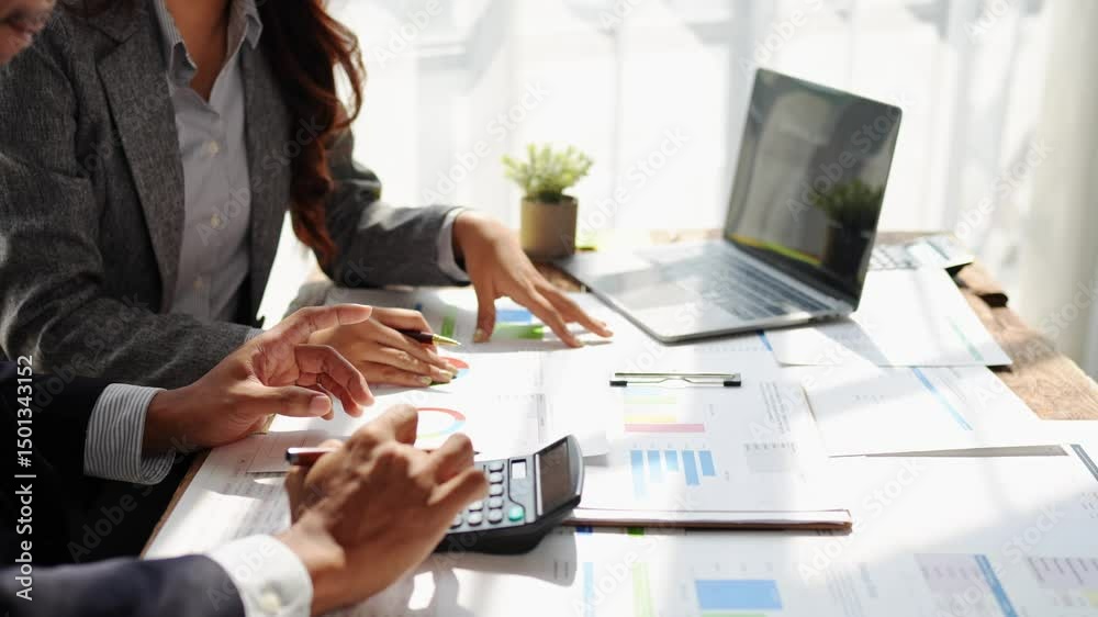 Young colleagues discuss business and analytical price charts using calculators and laptops to calculate financial, tax, accounting, statistics and analytical research ideas.