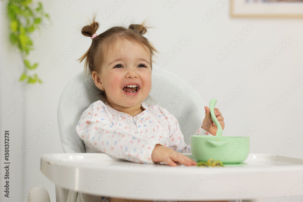 Cute little baby eating healthy food in high chair indoors Cute little baby eating healthy food in high chair indoors