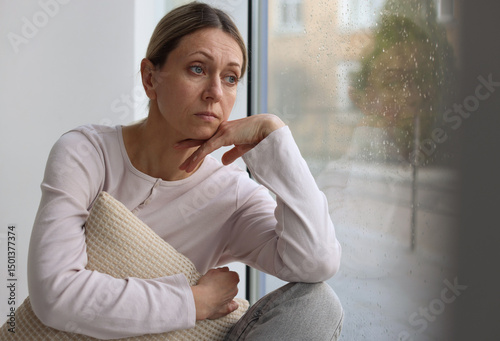 Fotografija Depressed woman looking out window at home, space for text