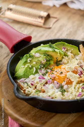 Fried egg with avocado, red onion, cheese, and crispy tortilla chips served in a cast iron skillet. Colorful and hearty breakfast close-up