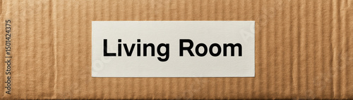 Closeup photo of cardboard box with label reading Living Room it, suggesting storage or organization home setting