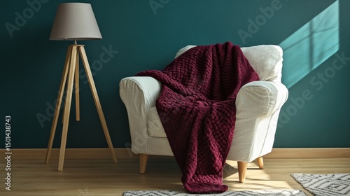 A maroon waffle-knit throw draped over a white armchair in a cozy room setting