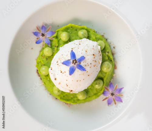 A fresh pea puree is beautifully plated, featuring a poached egg at the center and adorned with borage flowers. The dish showcases vibrant colors and textures, perfect for any spring menu.